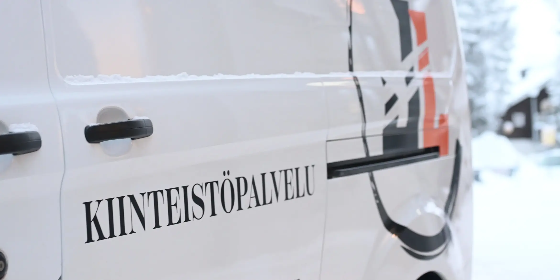 Valkoinen pakettiauto, jossa on teksti KIINTEISTÖPALVELU, on pysäköity lumiseen ympäristöön.